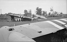 Photo en noir et blanc représentant des planeurs démantelés au sol, dans un champ, avec des arbres à l'arrière-plan.