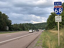 A four-lane freeway in a forested area with a sign saying East I-68. Snow Emergency Route.