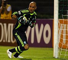 Um goleiro segurando uma bola de futebol com as duas mãos rente ao peito, de pé