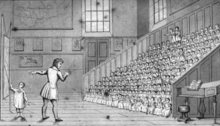 A teacher and his child assistant stand in front of a large class of children.