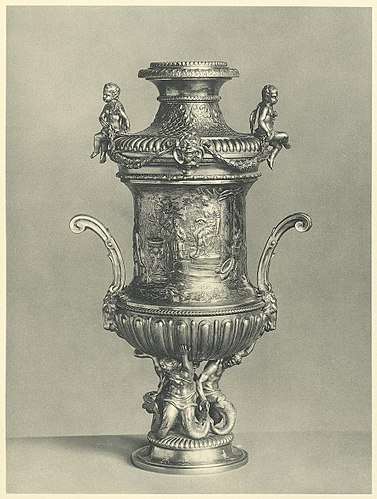 Hohe getriebene Vase von drei gegossenen Tritonen getragen. Der Mantel ist mit einem Tieropfer vor Diana und mit Aeneas am Eingang zur Unterwelt verziert. Von Abraham Drentwett d. Ä. in Augsburg um 1700