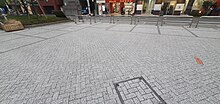 Petite place fait de pavés gris, certains pavés sont noirs pour montrer la forme de l'ancien bâtiment (et de ses pièces) qui formait la station de Senju