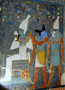 Painted relief of a seated man with green skin and tight garments, a man with the head of a jackal, and a man with the head of a falcon