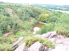 Des rochers rouges au premier plan, avec au fond un lac et la forêt.