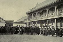 A photo of an assembly of staff in traditional Chinese clothing in front of a university hall