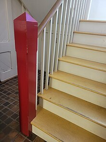 a simple red newel post at the base of blond wood and white stairs