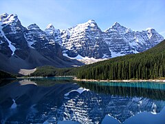 Sommets enneigés dominant des dépôts rocheux et se reflétant dans un lac turquoise.