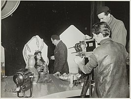 Opname voor de film in huis Te Manpad. Regisseur Schreiber vertelt prinses Tuuk wat er voor de volgende scene van haar verlangd wordt. Cameraman is Bert Haanstra.