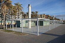 Foto einer Strandpromenade mit Palmen und Hotels, im Vordergrund zwei niedrige graugrüne Gebäude mit der Aufschrift Beach Club Six.