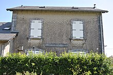 Photographie en couleurs de la façade du bâtiment de la gare avec deux fenêtres aux volets fermés.