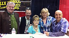 Five middle-aged Caucasoid adults (two women and three men) in casual dress are behind a table, posing for a group photo.