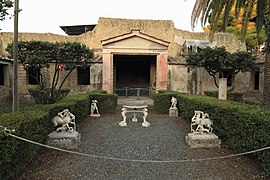 jardin décoré de sculptures blanches, au fond mur avec ouverture sous un fronton triangulaire