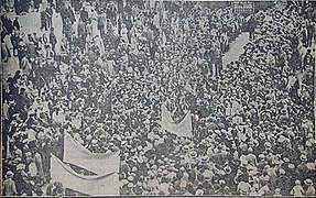 Photographie de presse en noir et blanc montrant une foule, vue en plongée. Quelques banderoles sont portées.