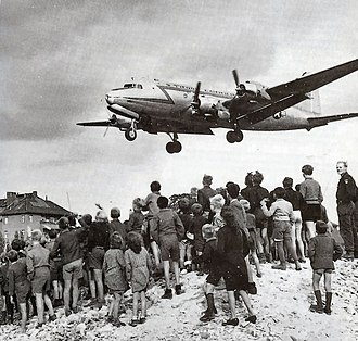 Ein Frachtflugzeug mit geöffneter Heckklappe wirft Frachtpaletten ab