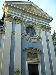 Vue d'une façade néoclassique bleue avec colonnades blanches et fronton décoré depuis la rue.