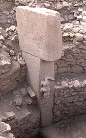 Pierre levée surmontée d'une autre. Les deux pierre forment un T et celle du dessous est partiellement enfoncée dans un mur en escalier de deux marches. Un animal est gravé en ronde bosse sur la pierre du dessous.