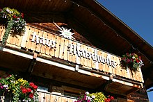 Großaufnahme auf die Stirnseite eines Gebäudes aus Holz, zwei Etagen; an der Brüstung des Obergeschosses große Schrift „Haus Matschwitz“