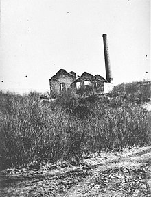 Deux bâtiments en ruine sans toiture et une grande cheminée.