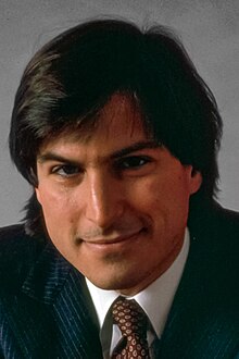 Steve Jobs smiles in a black suit.