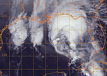 Black and white satellite image of a disorganized tropical cyclone in the Gulf of Mexico. Most of the storm's clouds are displaced to the north in an arc shape.