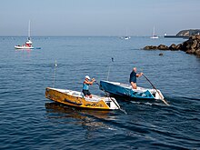 2 barques avec deux hommes qui se font la course à la godille en mer par beau temps