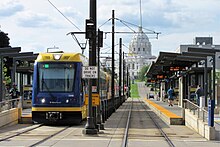 A three-car light rail at a station; the state capitol building is in the background.