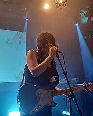 A woman with black pigtails singing into a microphone and holding an electric guitar