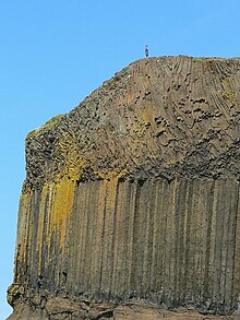 Cliff face showing three layers of rock; the bottom layer is sedimentary rock; the middle layer forms columns, whilst the layer above is blocky in appearance.