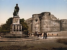 Photo d'une place pavée avec une statue en son centre, le château d'Angers en arrière-plan; deux petits attelages contournent la statue.