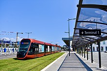 Vue d'un tramway traversant une place avec des arbres derrière.