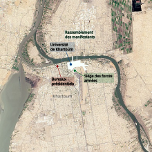 Image vectorielle en couleurs. Dans une image satellite de la ville de Khartoum, une surface blanche permet de localiser le sit-in dans le centre-ville. L'université de Khartoum se trouve dans la zone du sit-in, tandis que les bureaux présidentiels, à l'ouest, et le siège des forces armées, au sud-est, se trouvent proches de la zone, à l'extérieur.