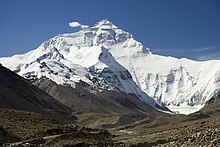 Sommet couvert de neige sous un ciel bleu vu depuis une vallée couverte de débris morainiques.