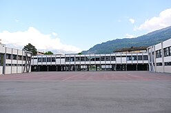 Bâtiment gris en fond d'une grande cour.