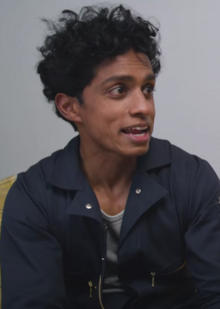 Rajiv Surendra wearing dark, zippered jacket, appearing to speak and looking left of camera