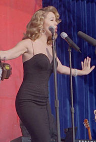 A woman in a black ensemble, performing a song at the filming of a music video.