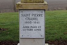 Plaque fixée sur le socle d'une statue (non visible), où est gravé en majuscules "Saint Pierre Chanel 1803-1841 Aimer Marie et la faire aimer".