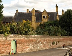 Yellow stone house with tall chimneys behind brick wall.