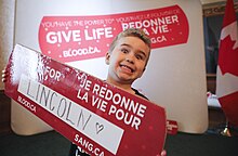 Boy holding a sign encouraging people to donate blood at the event