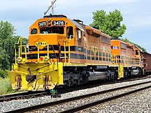 A pair of orange and black diesel locomotives parked on a siding, with train cars behind them.
