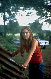 Actress Gina Philips grabs the edges of a large pipe; a car can be seen behind her.