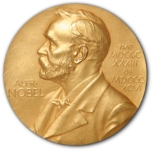 A golden medallion with an embossed image of a bearded man facing left in profile. To the left of the man is the text "ALFR•" then "NOBEL", and on the right, the text (smaller) "NAT•" then "MDCCCXXXIII" above, followed by (smaller) "OB•" then "MDCCCXCVI" below.