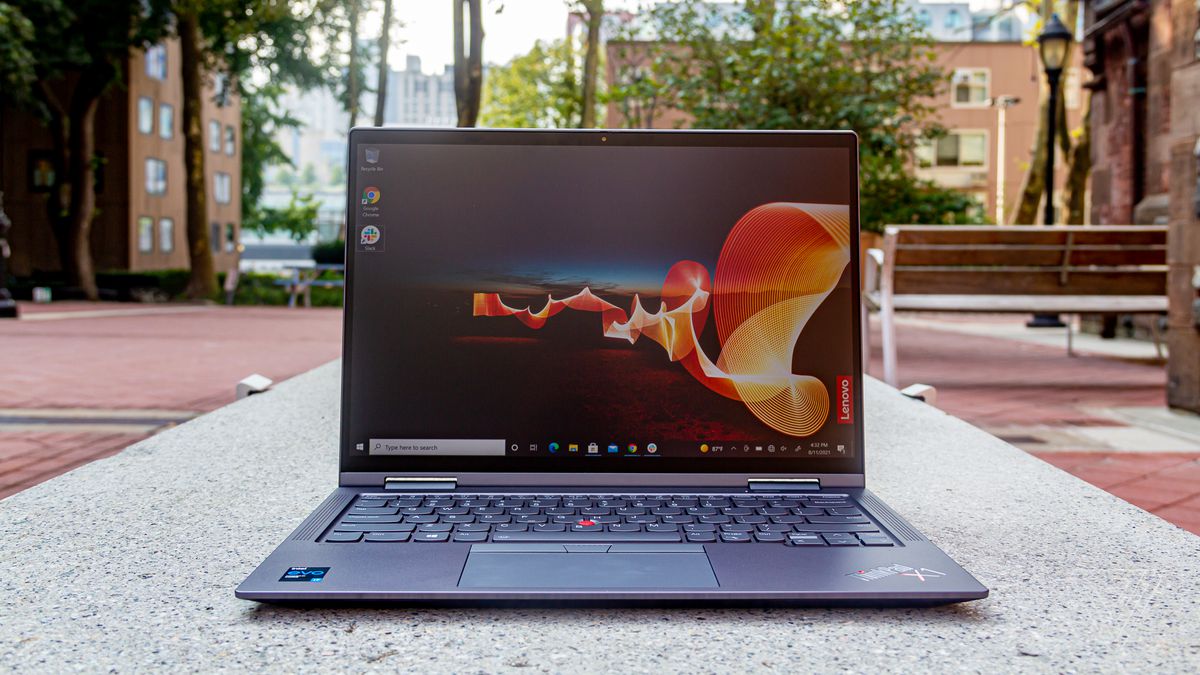 The ThinkPad X1 Yoga Gen 6 on a bench in an outdoor park, open. The screen displays an outdoor night scene with an orange banner rippling across it and the Lenovo banner on the bottom right side.