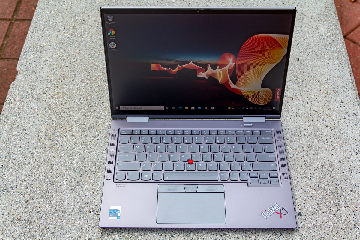 The Lenovo ThinkPad X1 Yoga Gen 6 open on a stone bench seen from above. The screen displays an outdoor night scene with an orange banner rippling through and the Lenovo banner on the bottom right side.