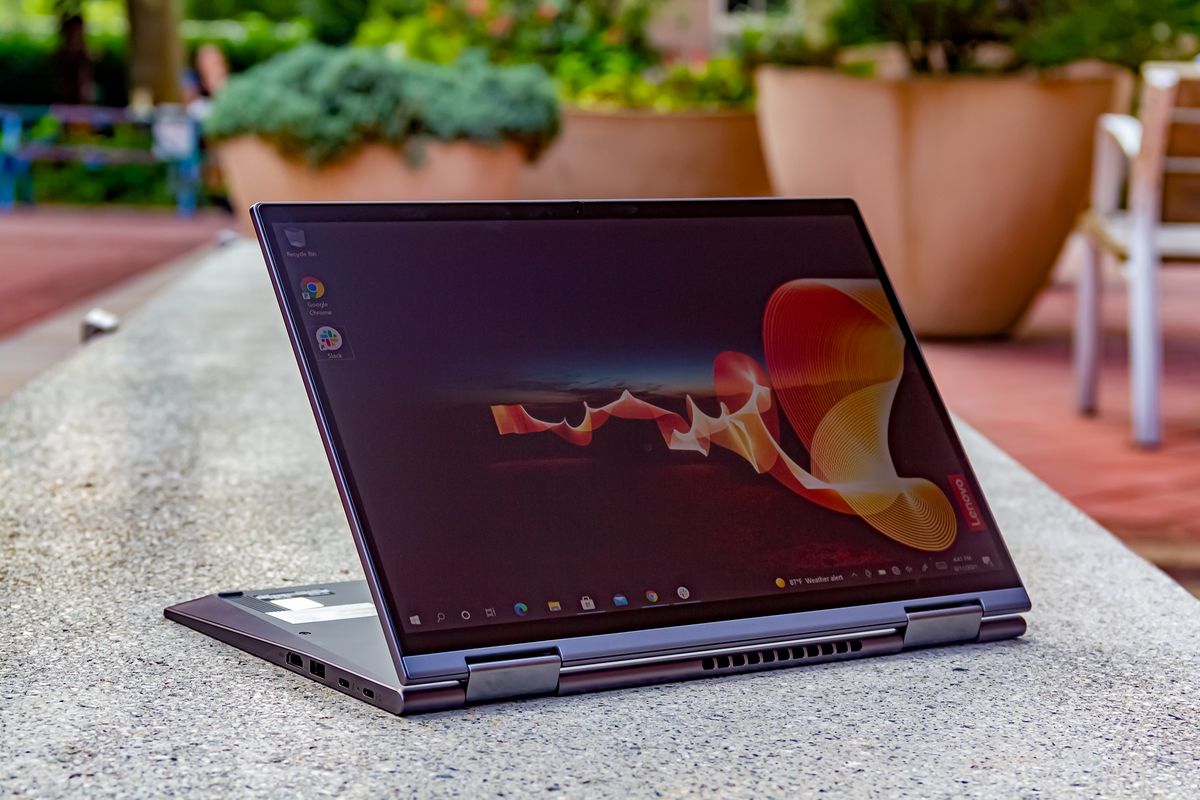 The Lenovo ThinkPad X1 Yoga Gen 6 in easel mode angled to the left on a stone outdoor bench. The screen displays an outdoor night scene with an orange banner rippling through and the Lenovo banner on the bottom right side.