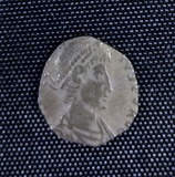 A small silver coin mostly consisting of a human head and shoulders. The shape is irregular and there is only a vestige of writing.