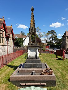 Colour photograph of Hill's grave at the front of the Methodist church in Churchill, North Somerset. The memorial has inscriptions on four sides. The view has the church to the left, with red railings surrounding the cemetery. Front street in Churchill is on the right of the picture.