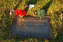 A flat, bronze grave marker surrounded by grass and decorated with flowers and small American flags