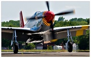 A single nosed-propeller aircraft is on the ground on its wheels with the propeller in motion. The aircraft is viewed from the front, but the red nose faces slightly to the right. The aircraft has black propellers. Parts of the wings and propellers are cropped from view.