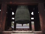 A large bronze bell with cross design hanging in an open roofed belfry.