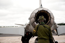 Headphone-wearing technician in green uniform, inspecting the engine nozzle of a single-engine fighter jet